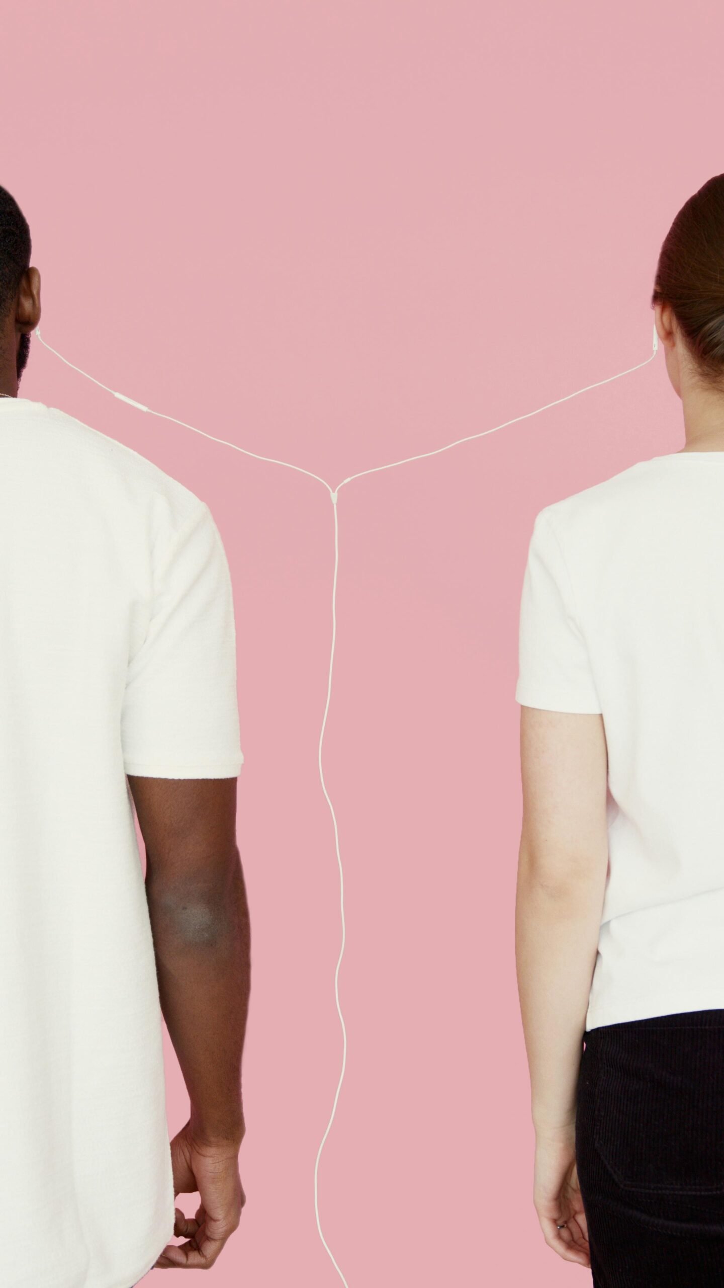 Two people connected by earphones against a pink background.